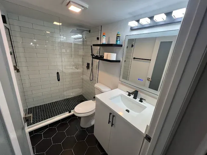 A modern bathroom with a white vanity, a walk-in shower with white subway tiles, and black hexagonal floor tiles.