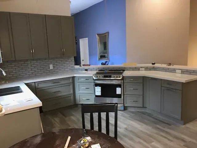 A modern kitchen featuring gray cabinets, white countertops, a gray tiled backsplash, and a stainless steel oven.