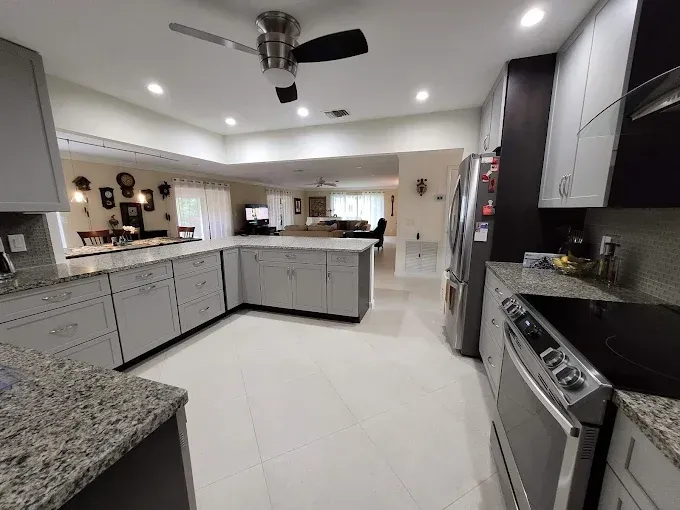 A wide-angle kitchen with gray cabinets, granite countertops, stainless steel appliances, and tile flooring.