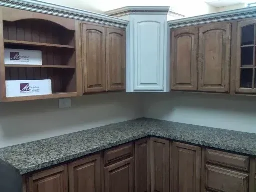 A kitchen corner with wooden cabinets, a light-colored corner unit, open shelves, and speckled granite countertops.