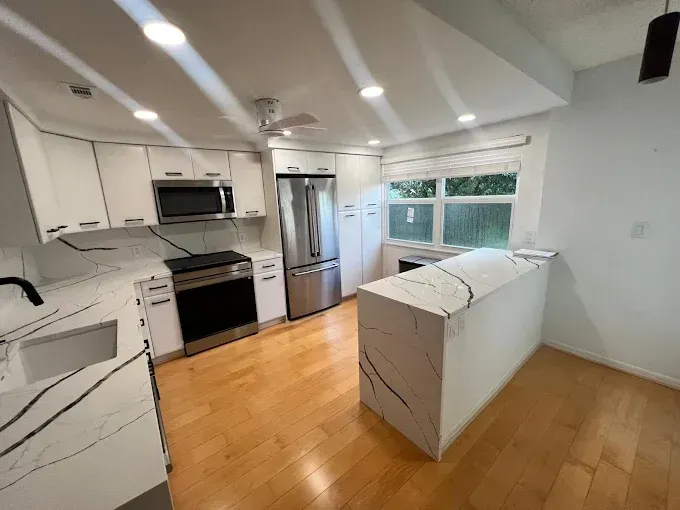 A modern, bright kitchen featuring white cabinets, stainless steel appliances, and marble-style countertops with black veining.