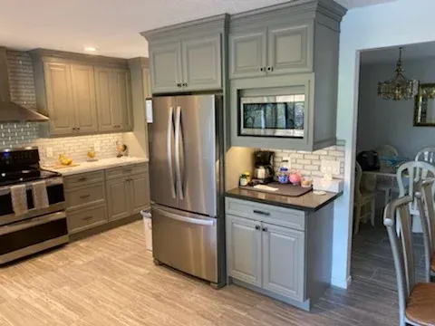 A modern kitchen with grey cabinets, stainless steel appliances, a tiled backsplash, and light-toned flooring.