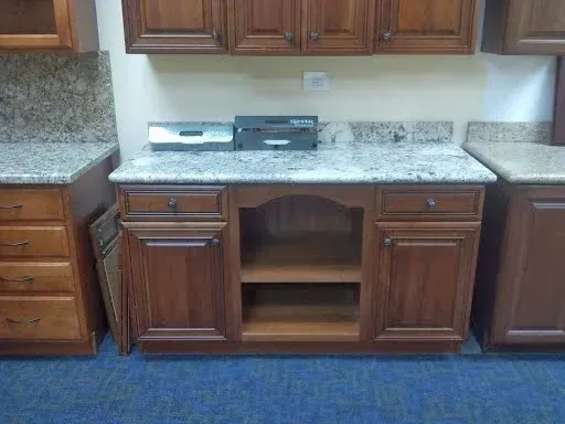 A wooden base cabinet with a granite countertop, featuring drawers, cabinets, and a central open shelf unit.