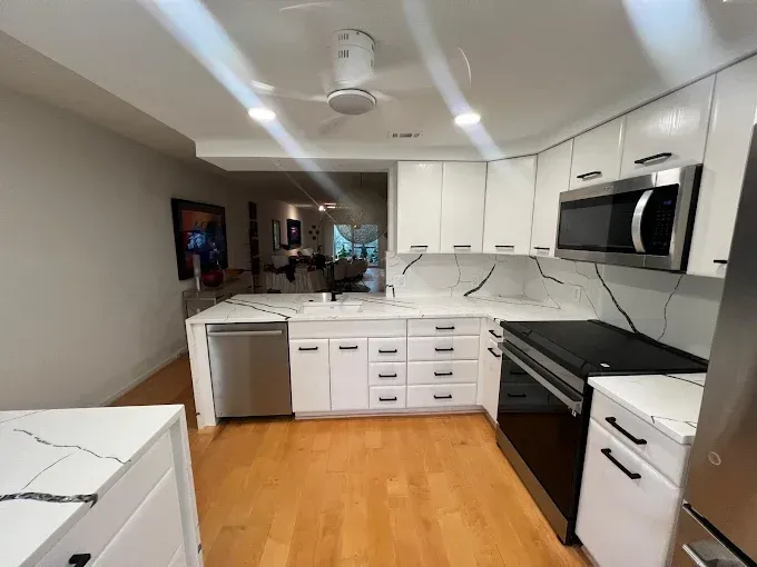 A modern kitchen featuring white cabinets, marble-patterned countertops, stainless steel appliances, and wood flooring.