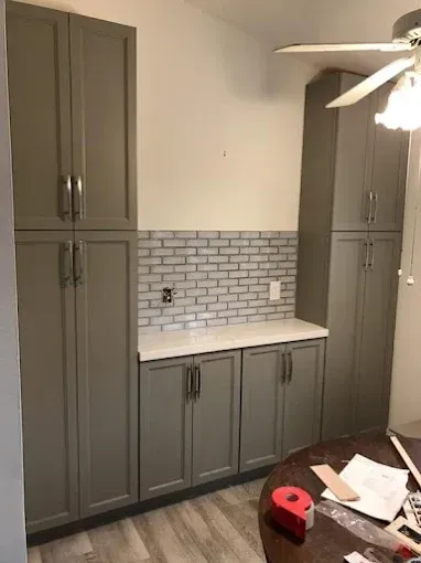 A gray built-in cabinet set with a white countertop and a light-gray brick-patterned backsplash in a home kitchen.