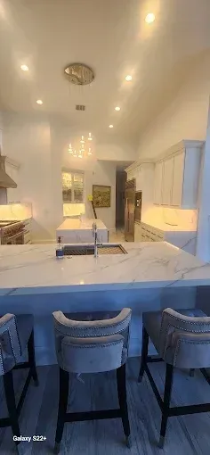 A modern kitchen with a white marble-topped island, gray bar stools, white cabinetry, and recessed lighting.