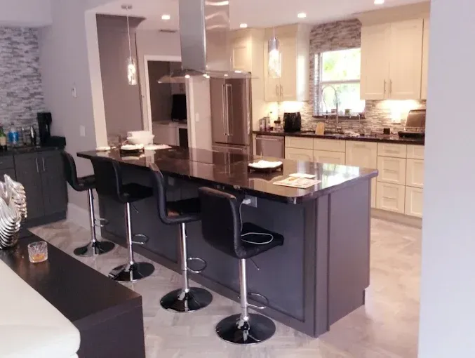 Modern kitchen featuring a dark island with three black bar stools, stainless steel appliances, and cream cabinetry.