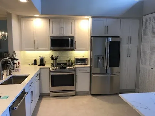 Modern kitchen with white cabinets, stainless steel appliances, a center stove, and white stone countertops.