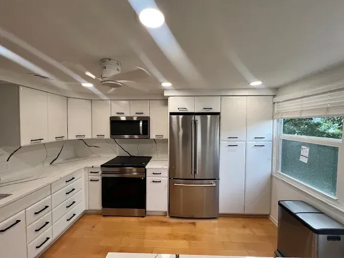A modern kitchen with white cabinets, stainless steel appliances, a black stove, and light wood floors.