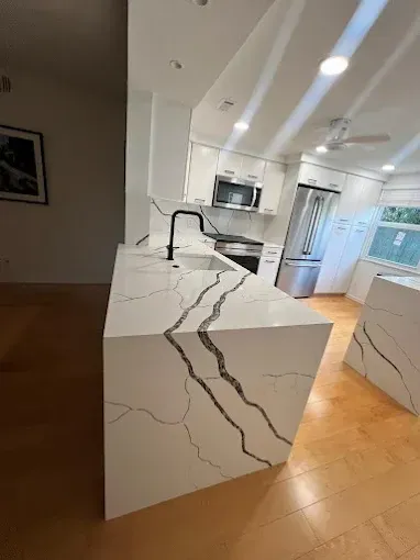 Modern kitchen featuring a white quartz island with bold grey veining, matte black faucet, and hardwood flooring.