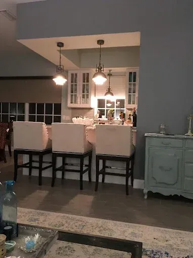 A kitchen island with three white stools under two pendant lights, set against a grey wall with a light blue cabinet.