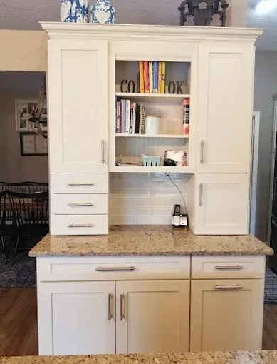 Cream-colored kitchen cabinetry featuring upper shelves with cookbooks, a granite countertop, and lower cabinet storage.