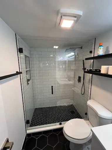 A modern bathroom featuring a glass shower with white subway tiles and black hexagon floor tiles, next to a white toilet.
