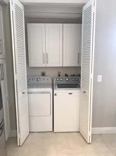White washer and dryer inside a closet with folding doors and overhead white storage cabinets.