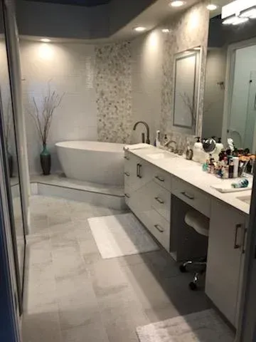 Modern bathroom featuring a white freestanding tub, gray tile floors, and a double vanity with a large mirror and lighting.