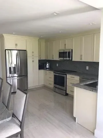 A kitchen with cream-colored cabinets, stainless steel appliances, and gray countertops, featuring an open floor plan.