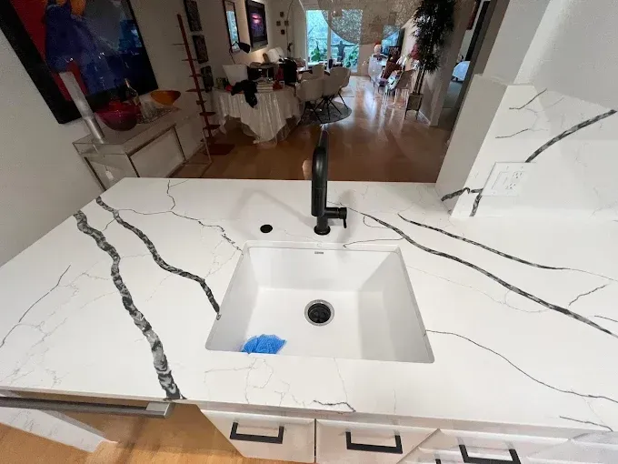 A modern kitchen island with white, black-veined quartz countertops, a white undermount sink, and a black faucet.