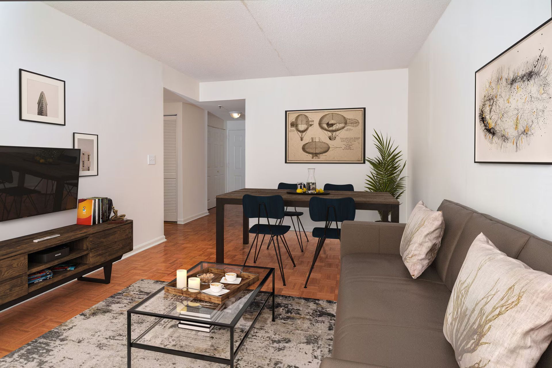 Living room with a dark wooden table and chairs, a brown sofa, and a TV on a console. Contact us to take a tour of our studio, 1, and 2-bedroom apartments for rent in New Brunswick, NJ today!