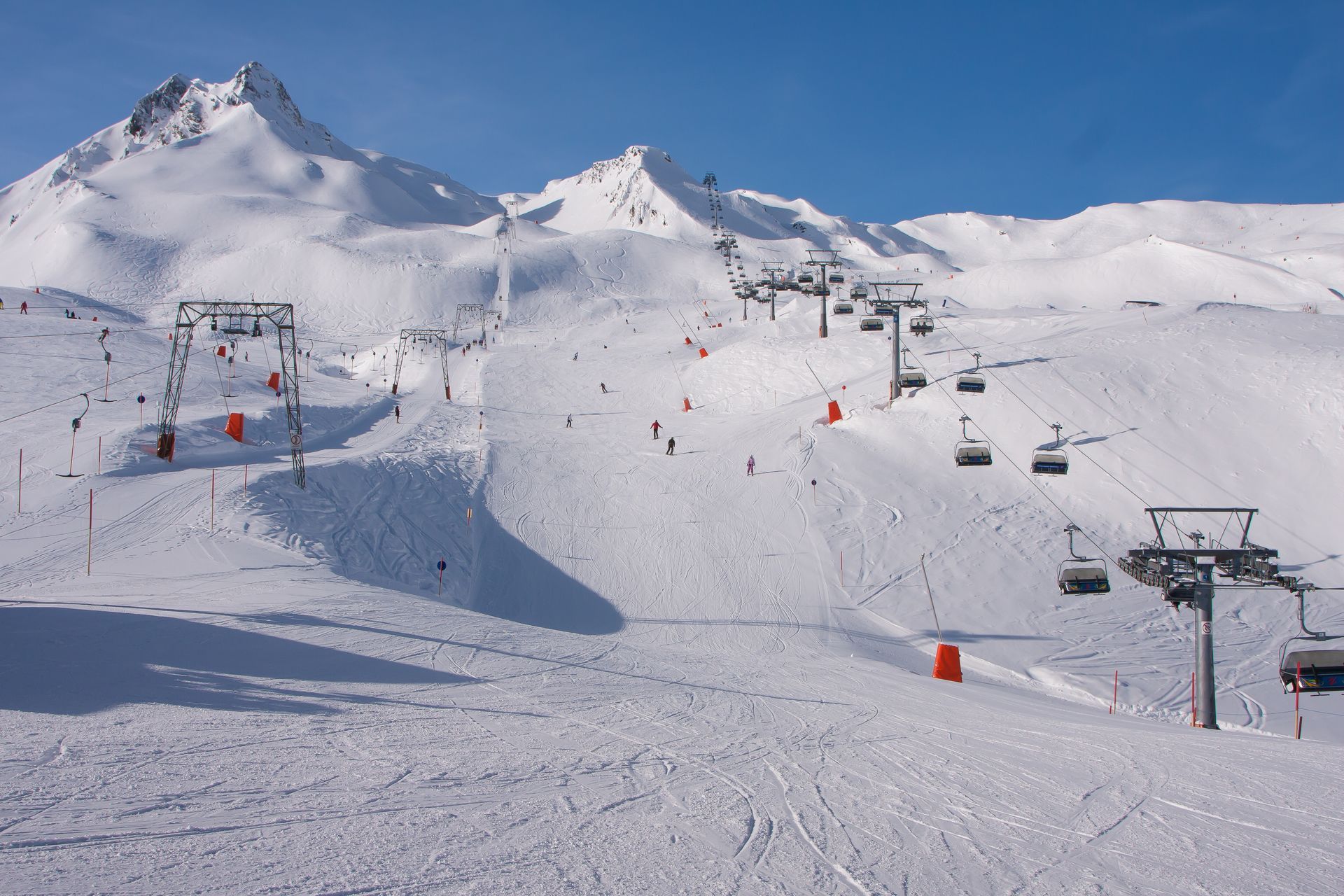 Skipiste mit Sesselliften, schneebedeckte Berge und Skifahrer an einem hellen, sonnigen Tag.