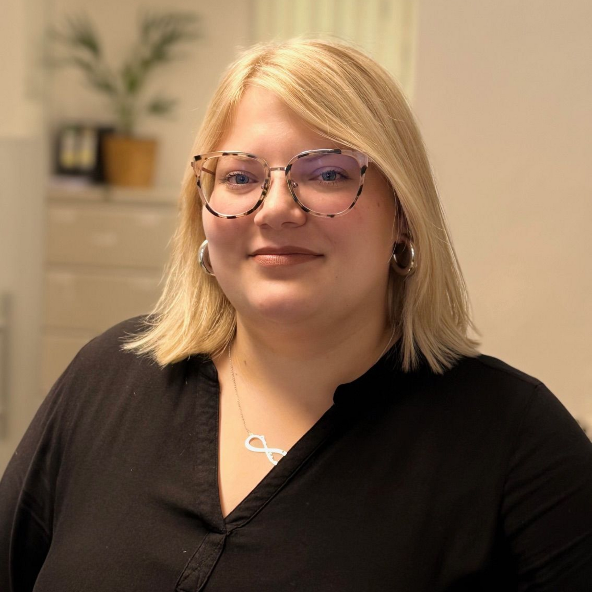 Frau mit blonden Haaren, Brille und schwarzem Hemd, lächelnd.