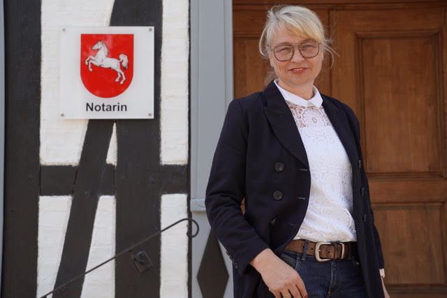 Frau im Blazer steht neben Gebäude mit „Notarin“-Schild.
