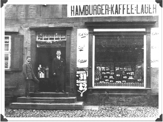 Ein Schwarzweißfoto von zwei Männern vor einem Laden namens Hamburger Kaffee
