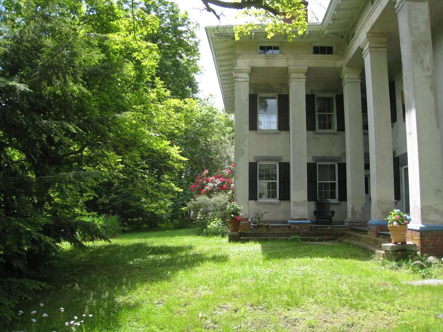 A large white house with black shutters is surrounded by trees