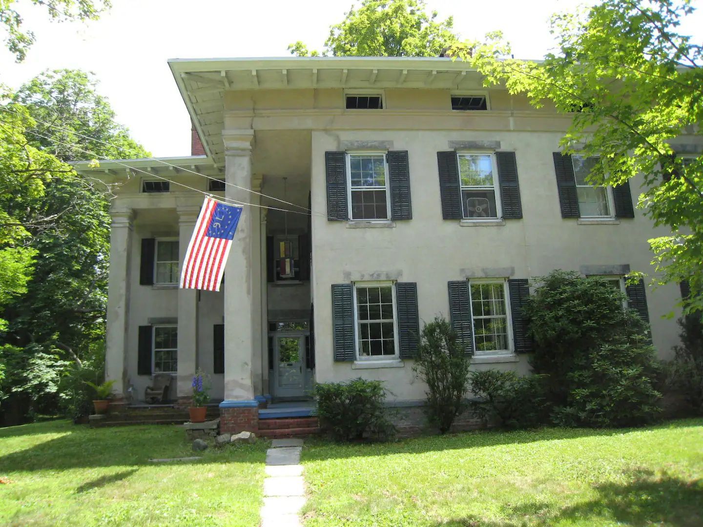 A large white house with black shutters and an american flag on the porch