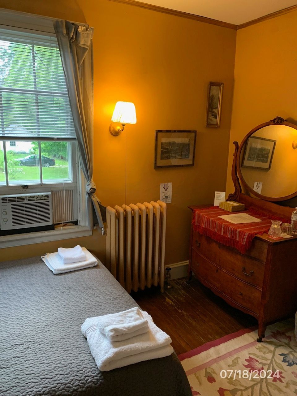 Cozy yellow room with a bed, window, dresser, and radiator.