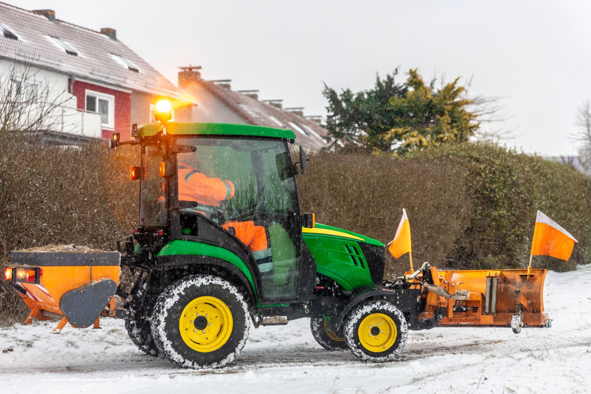 Green tractor with plow clearing snow on a residential street during a snowfall