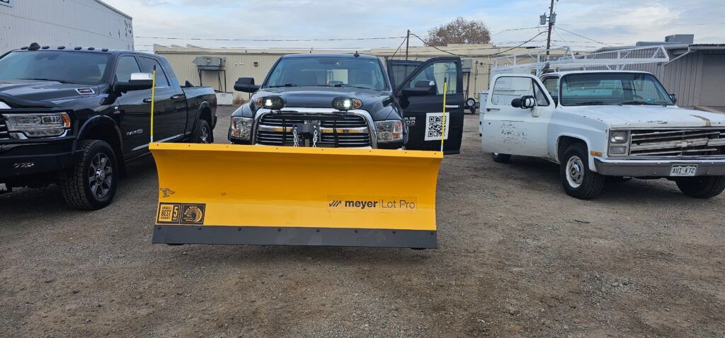 A group of trucks and a snow plow are parked in a gravel lot.