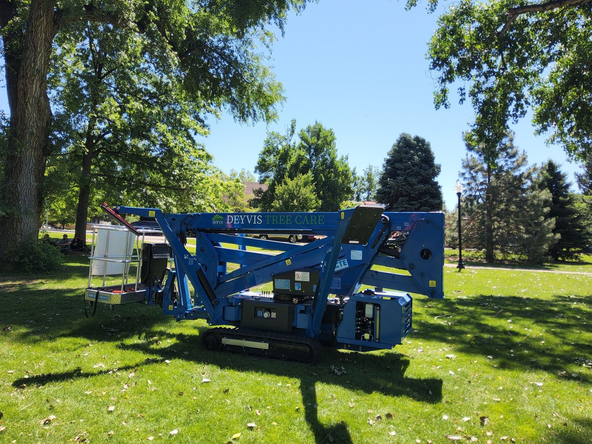 A blue aerial lift is parked in the grass in a park.
