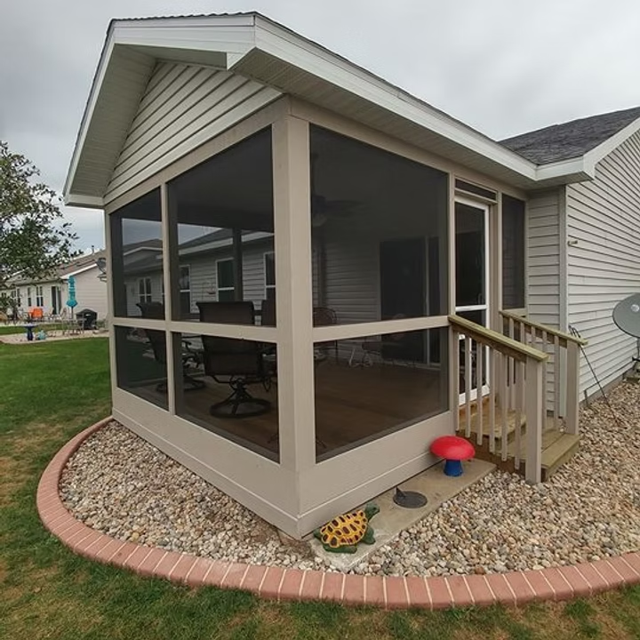 Screened porch with beige siding, small steps, and curved brick edging in a yard