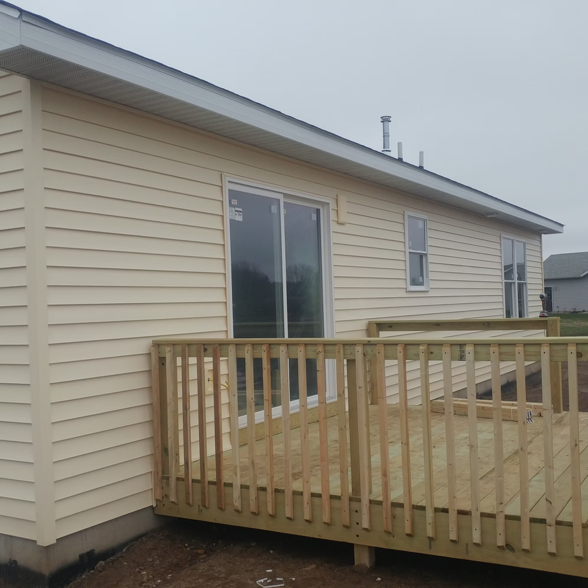 Beige house exterior with a wooden deck and sliding glass door under a cloudy sky