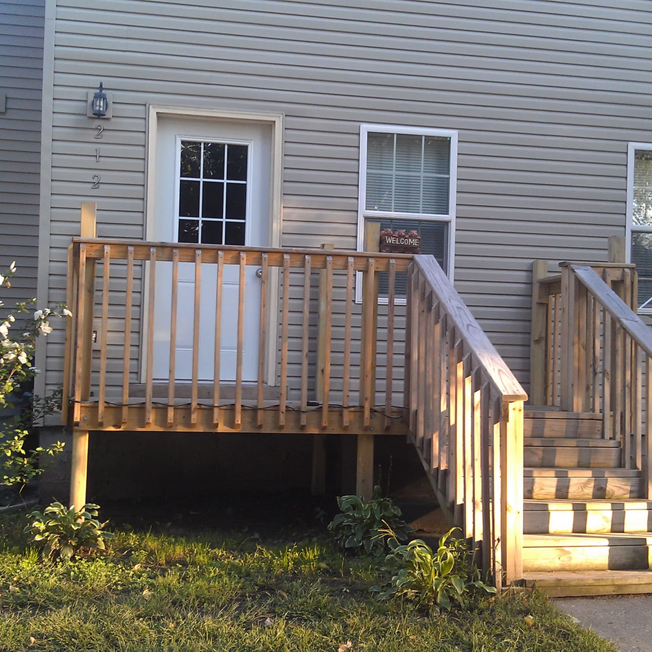 Wooden back deck with stairs beside a beige house and white-framed door and window