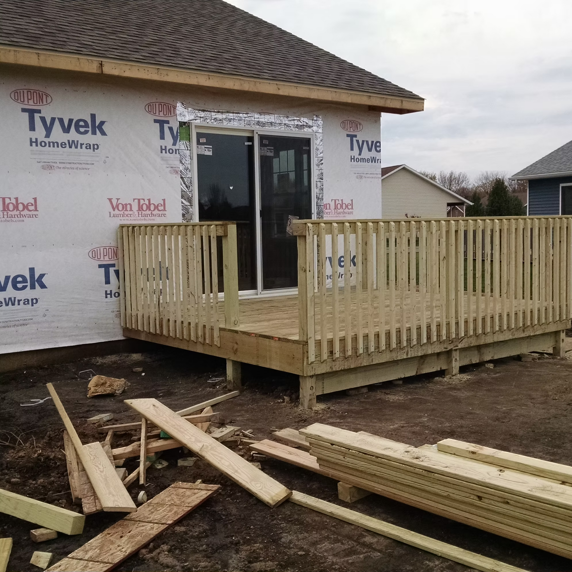 House under construction with Tyvek wrap and a newly built wooden deck and railing in front.