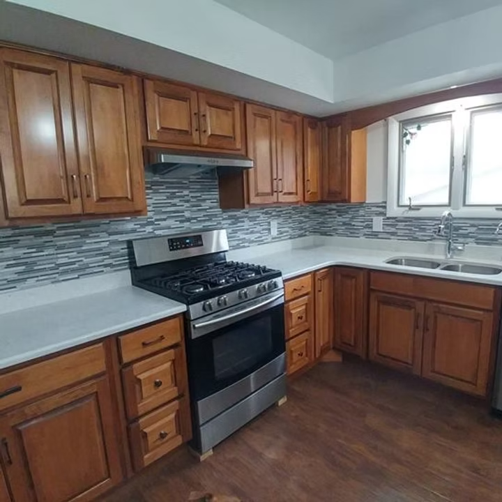 Modern kitchen with wooden cabinets, stainless steel stove, gray countertops, and tiled backsplash