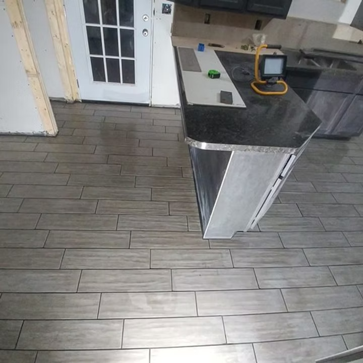 Kitchen with gray tile floor, black countertop island, white door, and a small light on the counter.