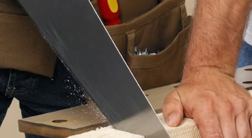 Close-up of a hand sawing wood with a hand saw in a workshop