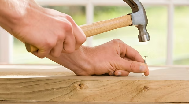 Hand using a hammer to drive a nail into a wooden board