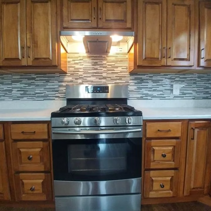 Modern kitchen with stainless steel stove, wood cabinets, and mosaic tile backsplash