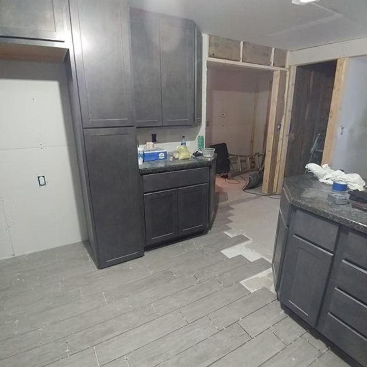 Unfinished kitchen with dark cabinets, gray floor, exposed wall framing, and a white door.