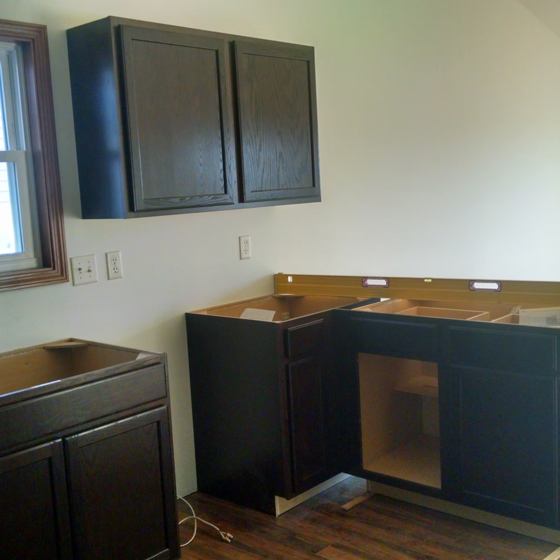 Empty kitchen with dark cabinets, wood countertop, sink, and window light under construction.