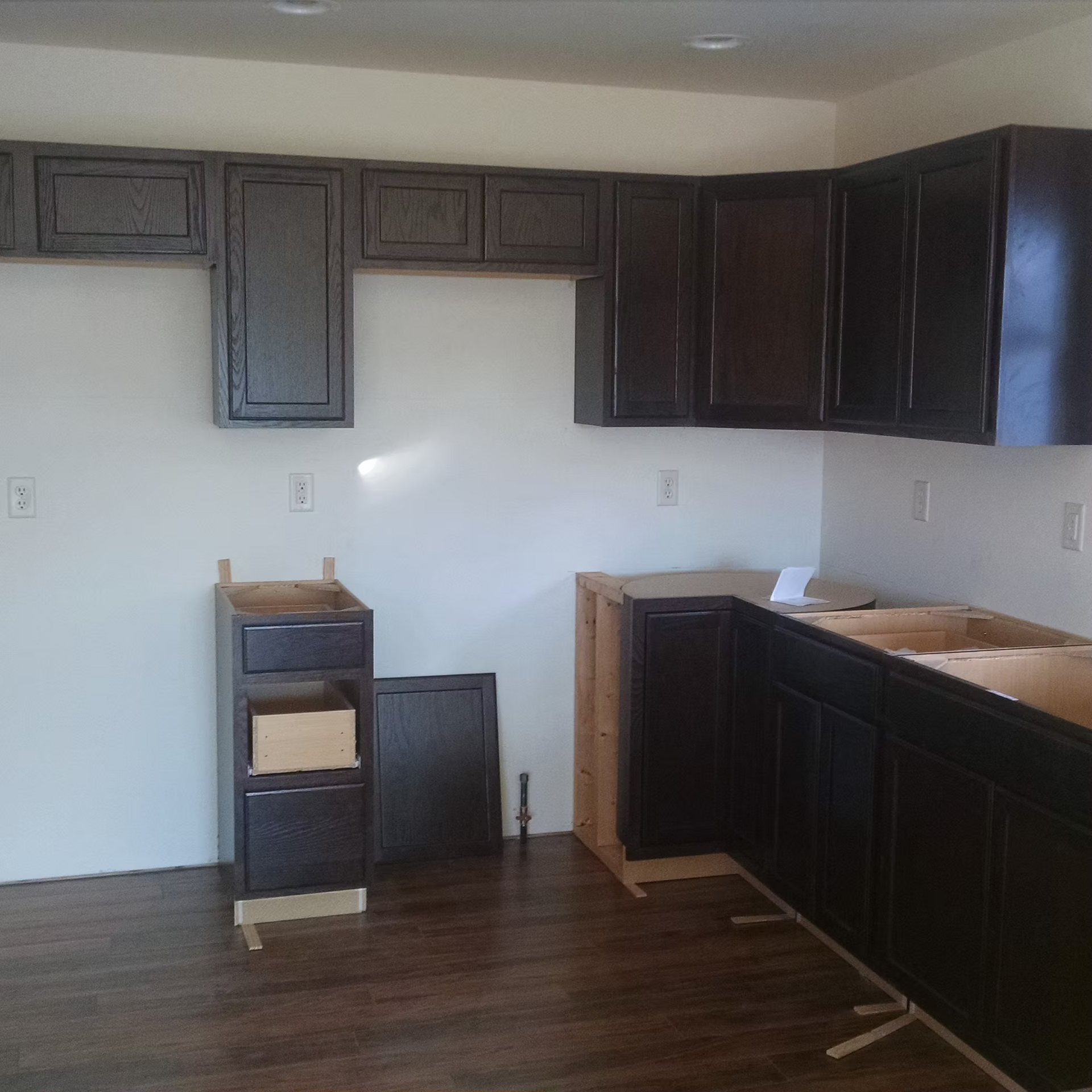Unfinished kitchen with dark cabinets, brown floors, and a white wall backsplash area