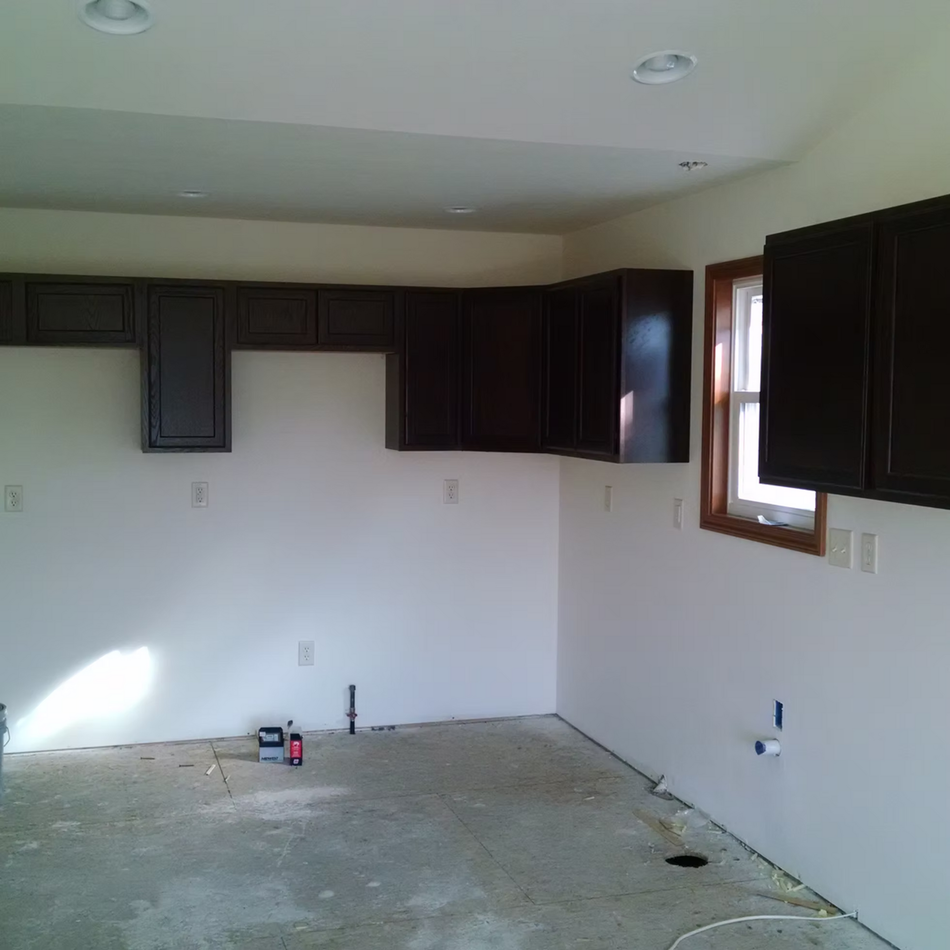 Empty kitchen with dark cabinets, white walls, a window, and bare concrete floor under renovation