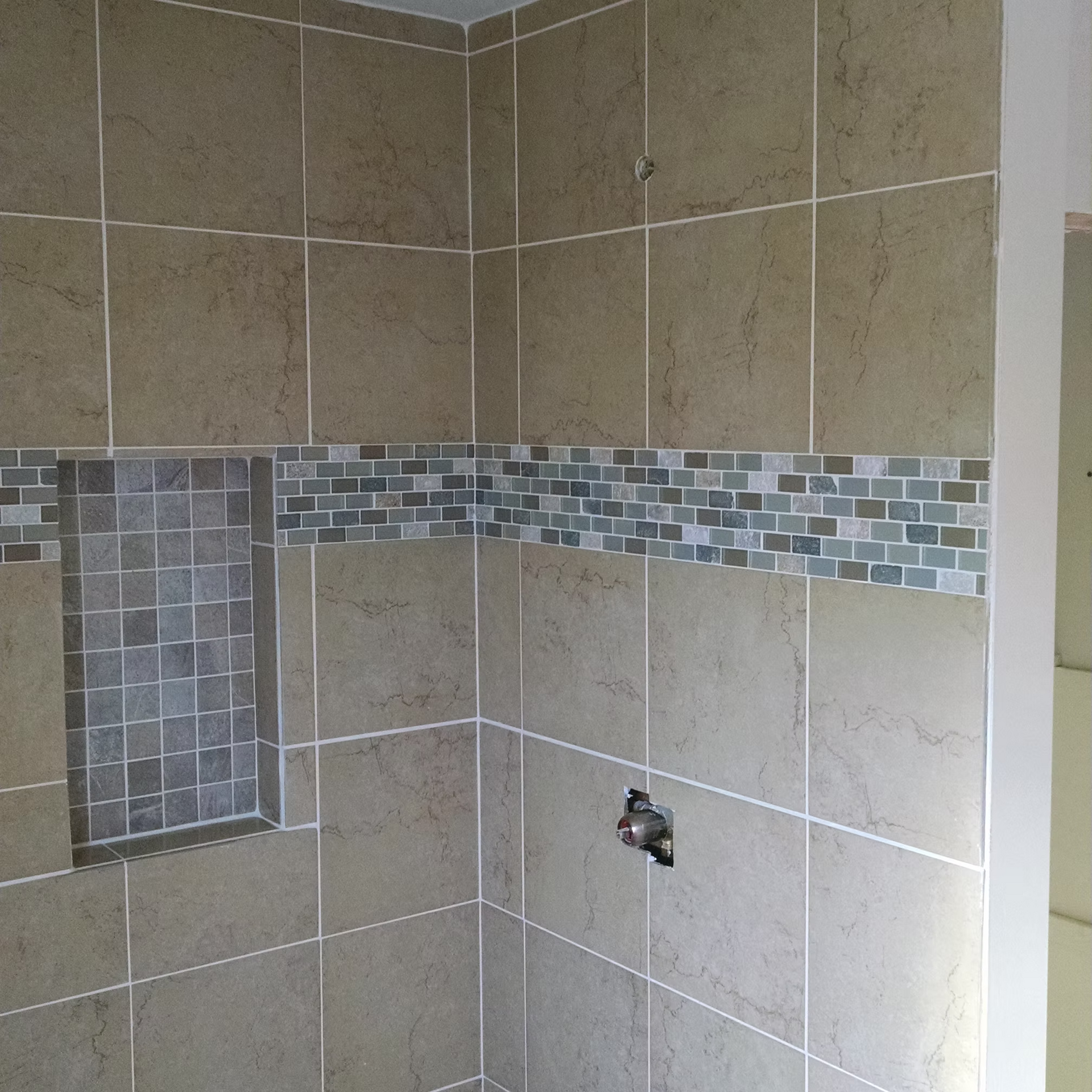Tiled bathroom shower wall with gray-beige tiles and a blue-gray mosaic accent strip