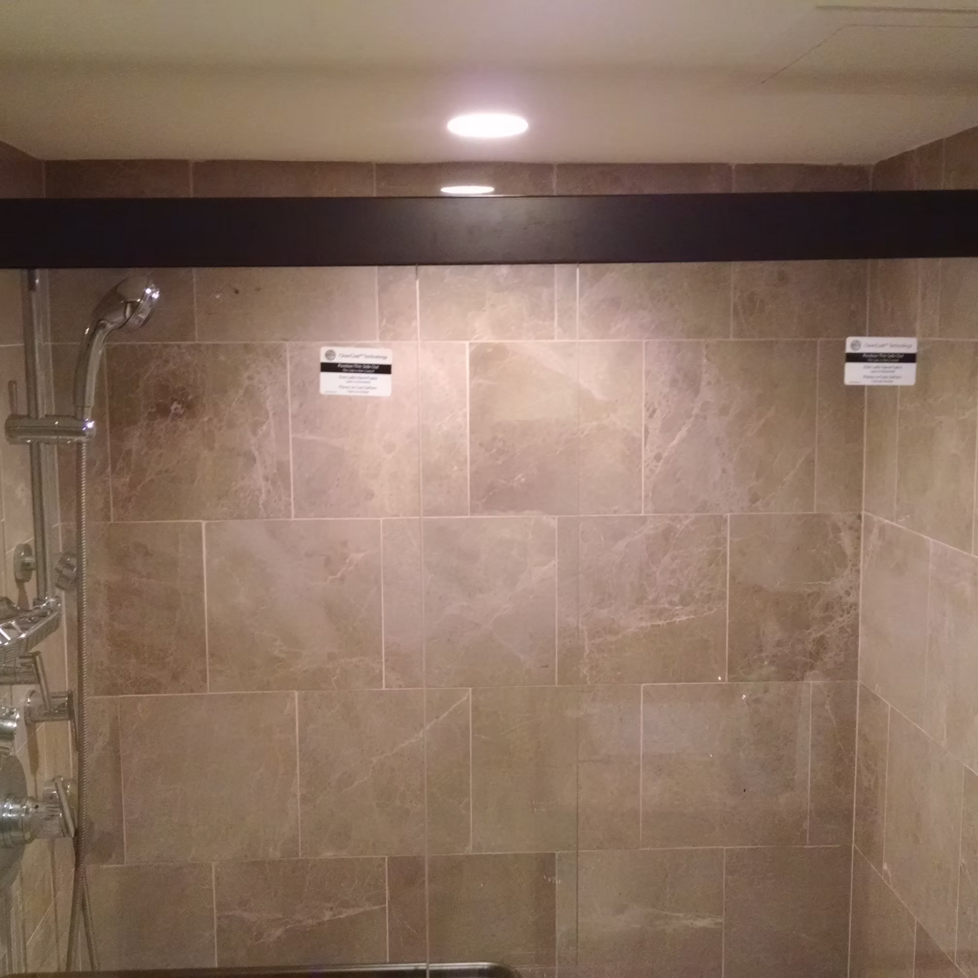 Empty tiled shower with a chrome handheld showerhead and two wall signs under recessed lighting