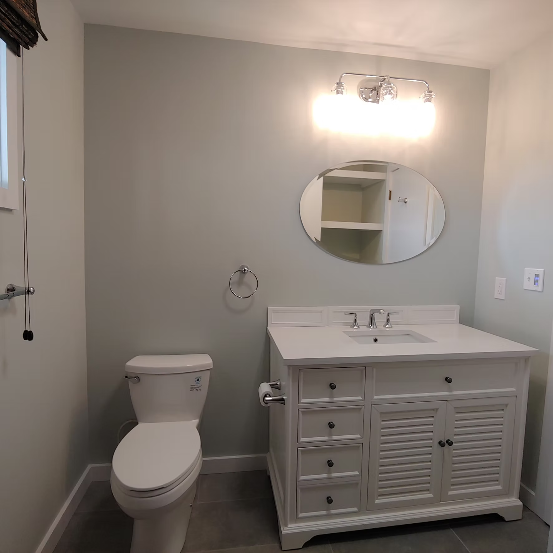 Small bathroom with a toilet, vanity sink, mirror, and wall light in light gray tones