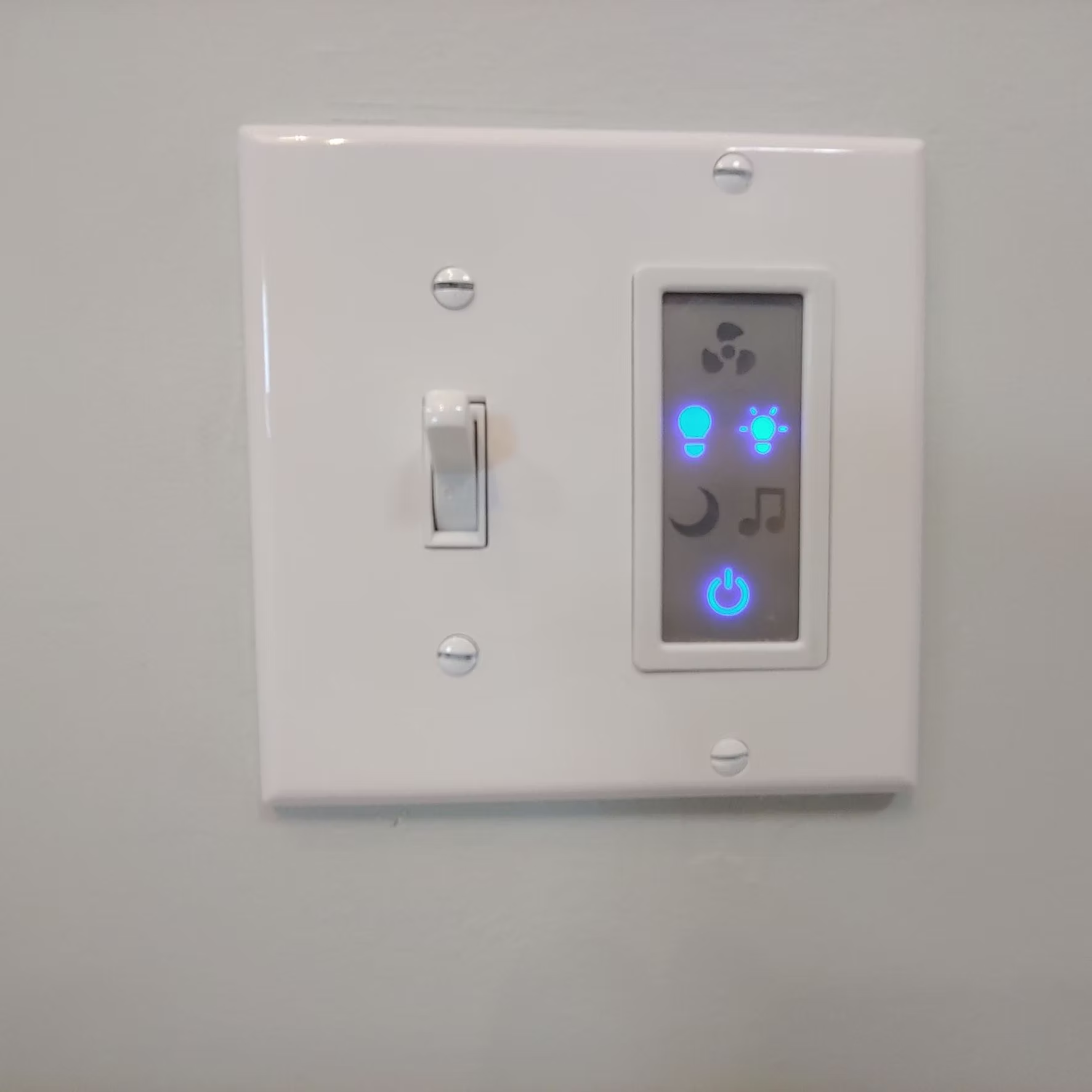 Wall switch and illuminated smart control panel on a white wall.