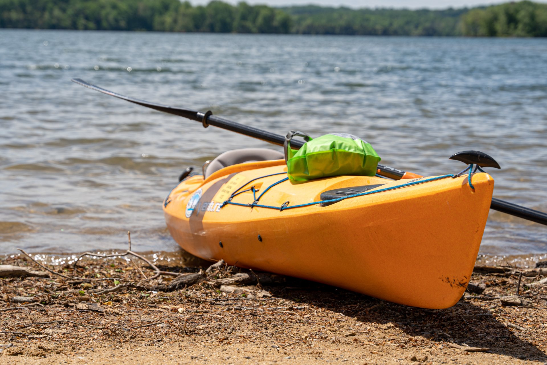 A yellow kayak is sitting on the shore of a lake with a fishing rod attached to it.